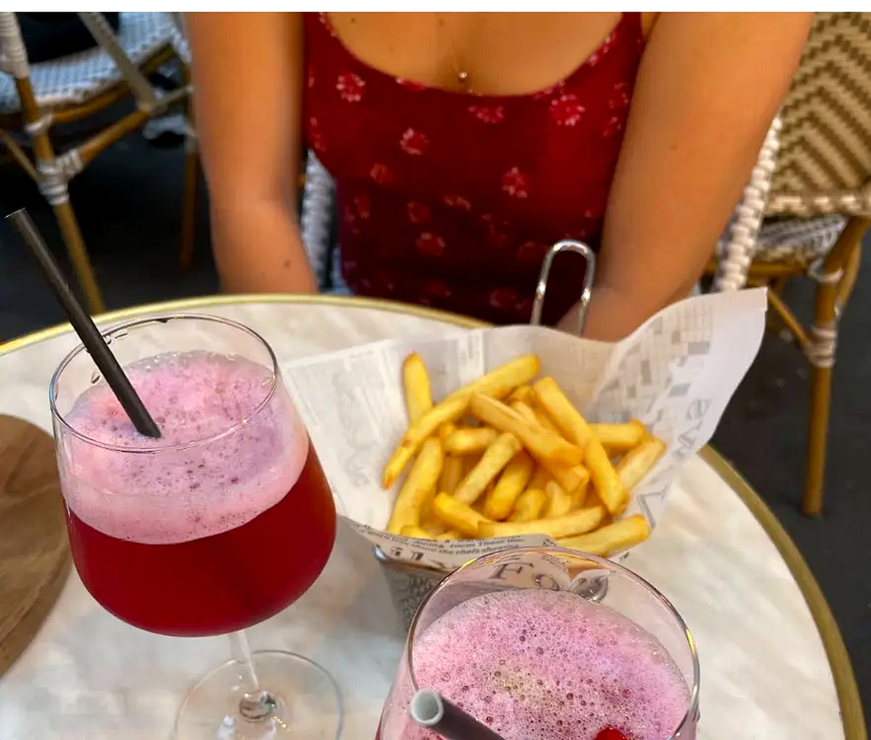 Cocktail rose et cornet de frites sur une table en terrasse